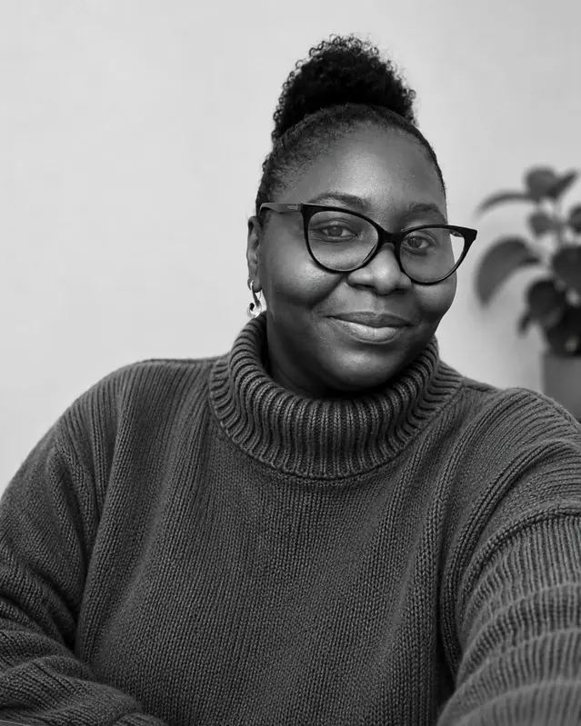 Tee Obi, smiling, wearing glasses and a dark jumper